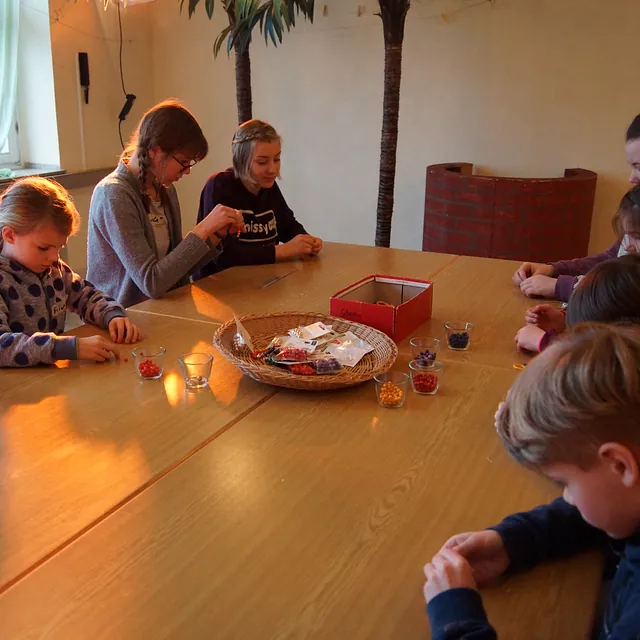 Die Kinder fädeln bunte Perlen für ein Armband auf