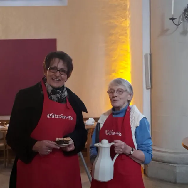 Zwei Damen aus der Gemeine mit roten Schürzen mit den Texten Plätzchen-Fee und Kaffee-Fee.